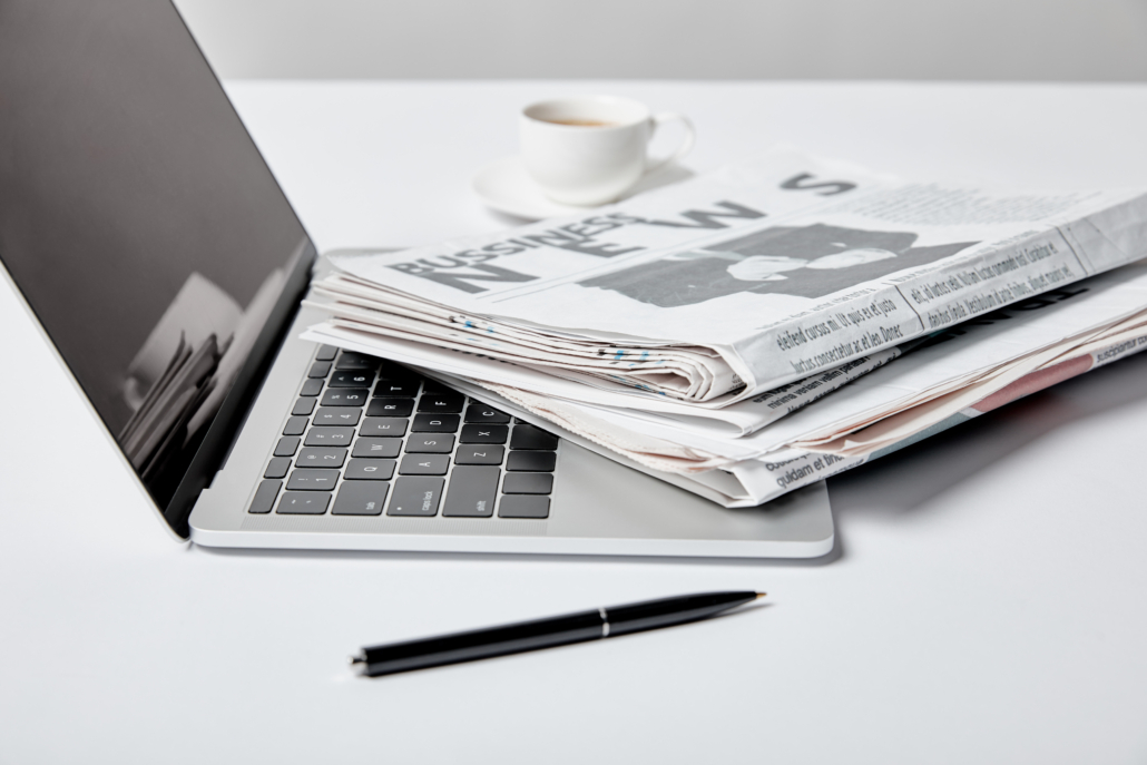 selective focus of laptop with blank screen near business newspapers, pen and cup